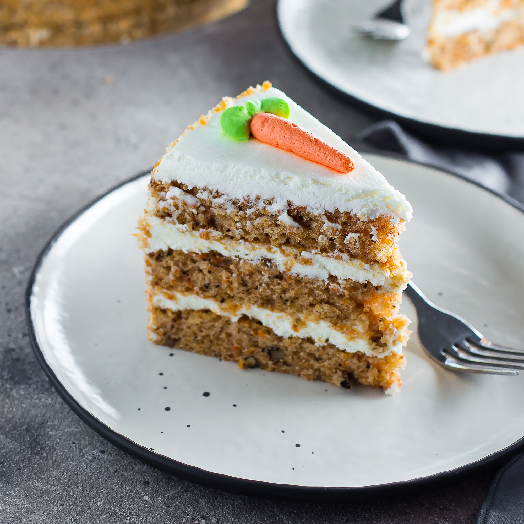 Slice of homemade carrot cake with cream cheese frosting on plate on gray stone table background.