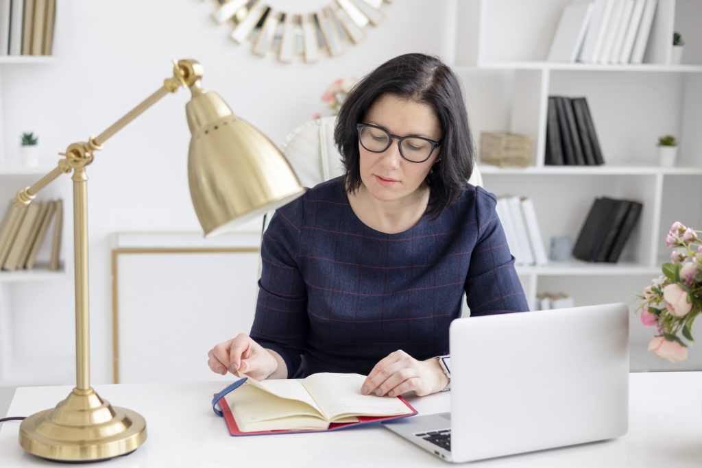 a young woman in glasses and in a blue shirt works at home at a laptop as a coach
