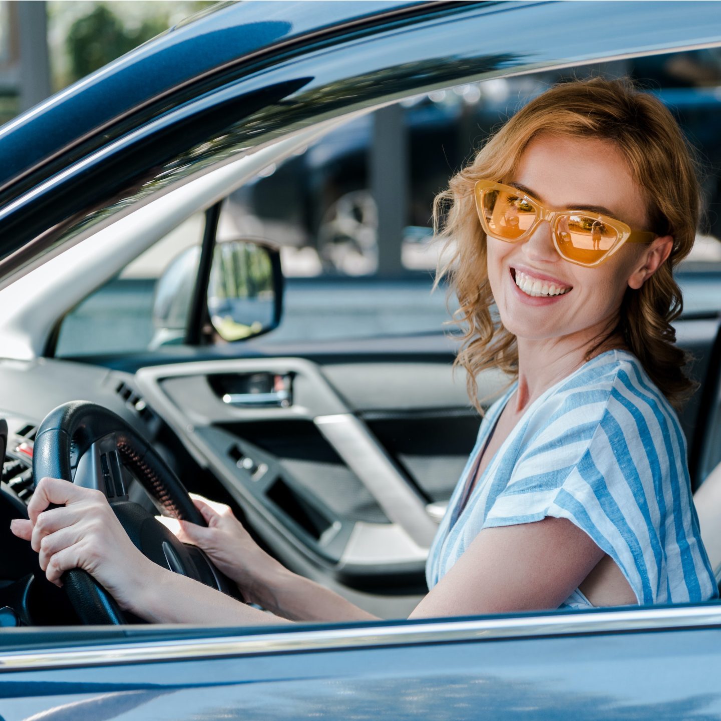 happy woman in yellow sunglasses holding steering wheel in car