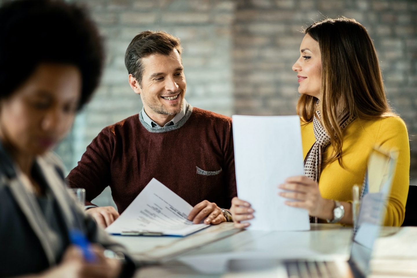 Happy couple consulting each other while being on a meeting with financial advisor.