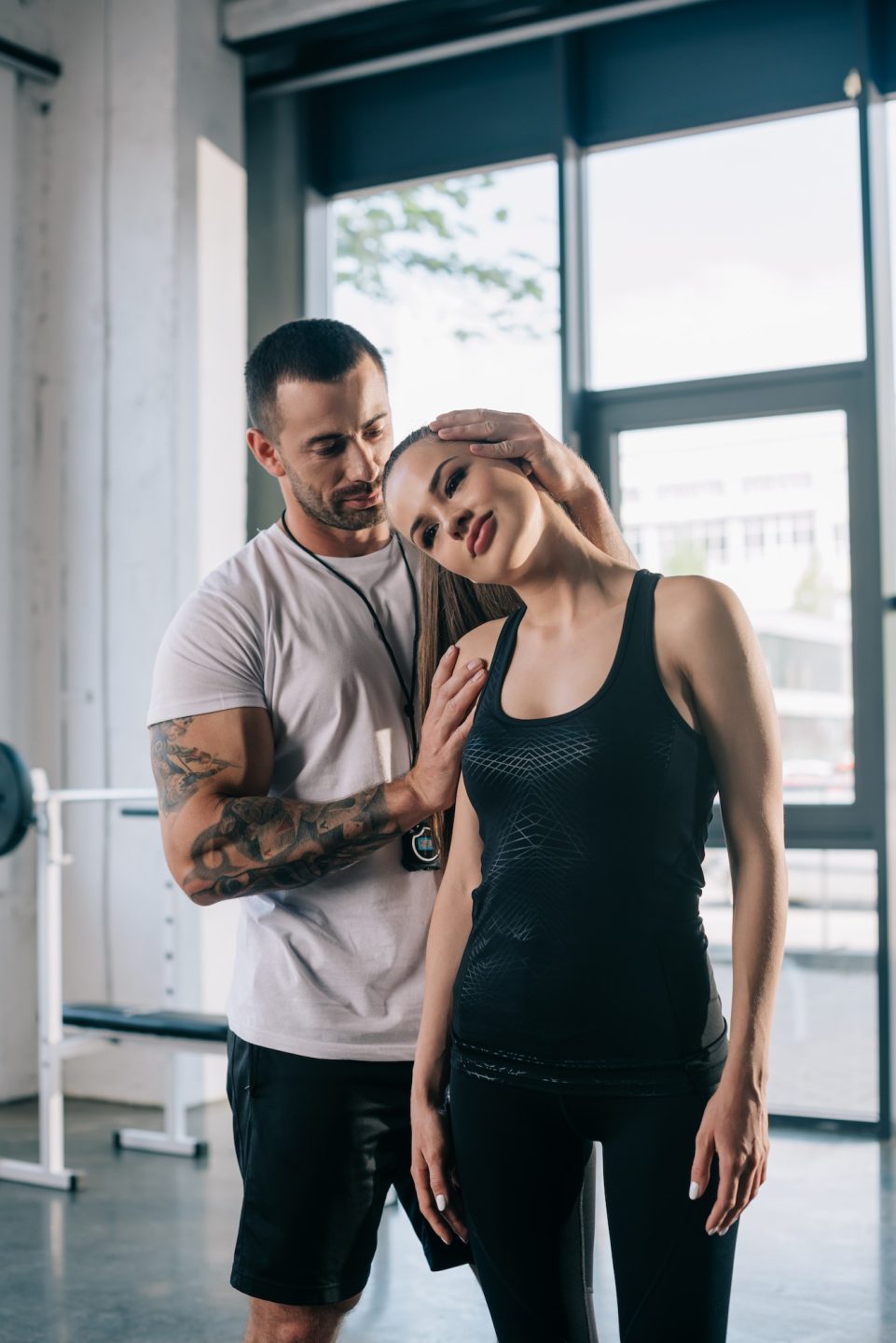 male personal trainer helping sportswoman to stretching at gym