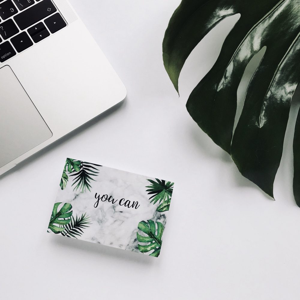 Top view laptop on white background desk with postcard monstera texture inspirational quote You can