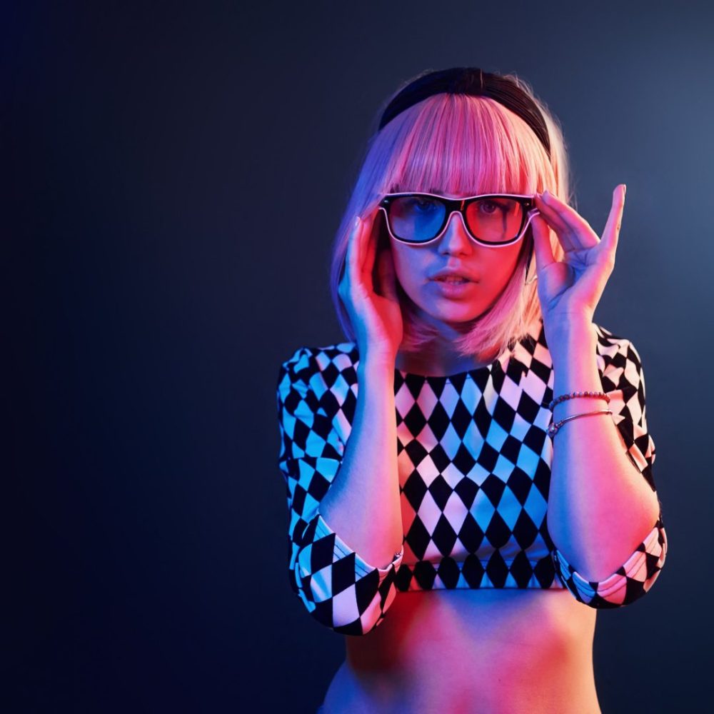 Portrait of young girl with blond hair in eyeglasses in red and blue neon in studio