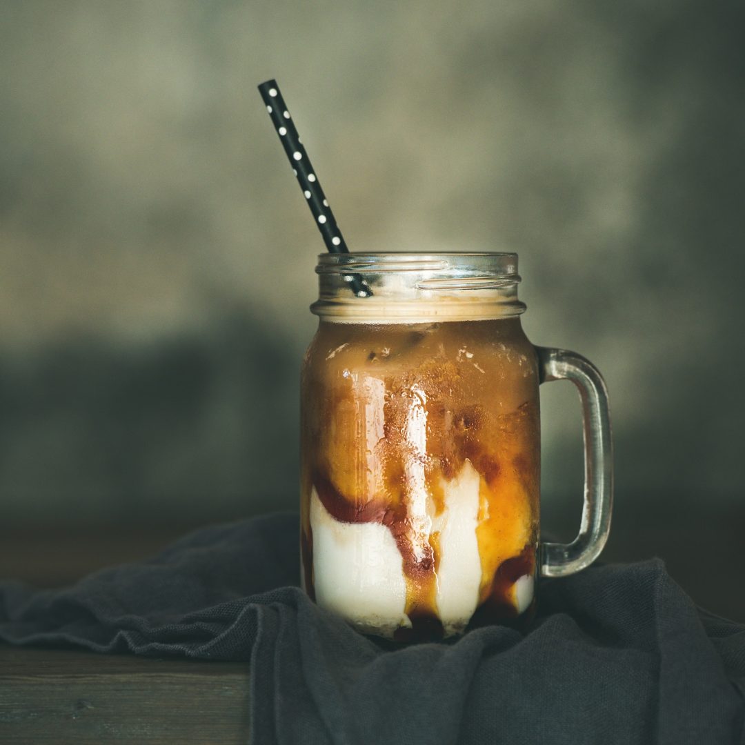 Iced caramel macciato with milk in glass jar, square crop