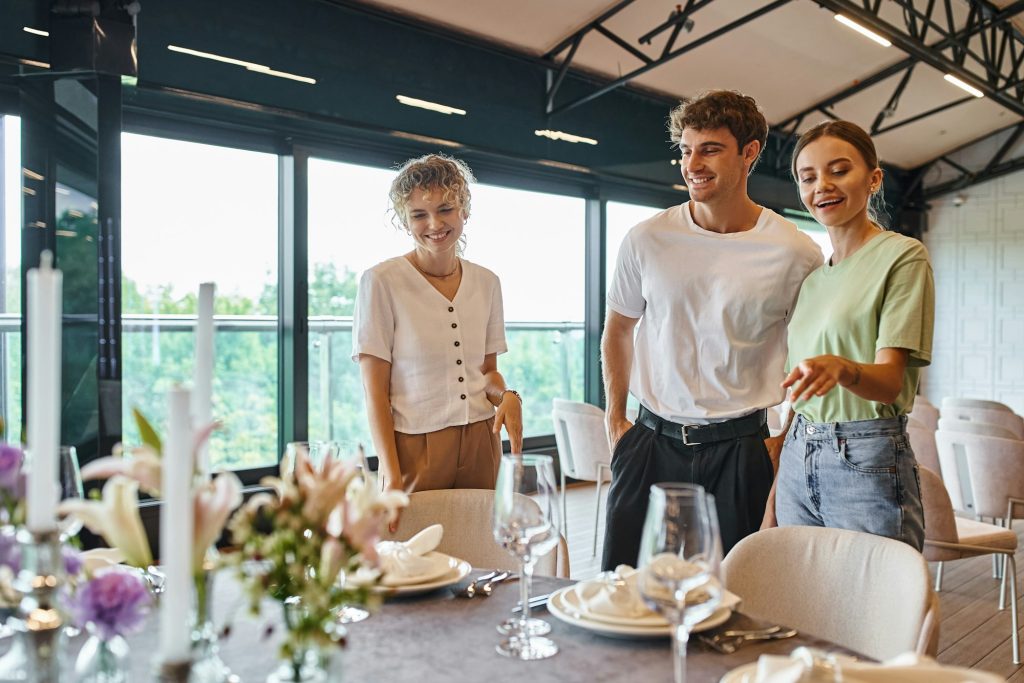 smiling team lead pointing at decorated festive table and talking to decorators in event hall