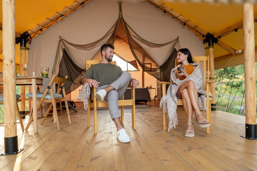 Young relaxed couple sitting in armchairs on patio of glamping tent