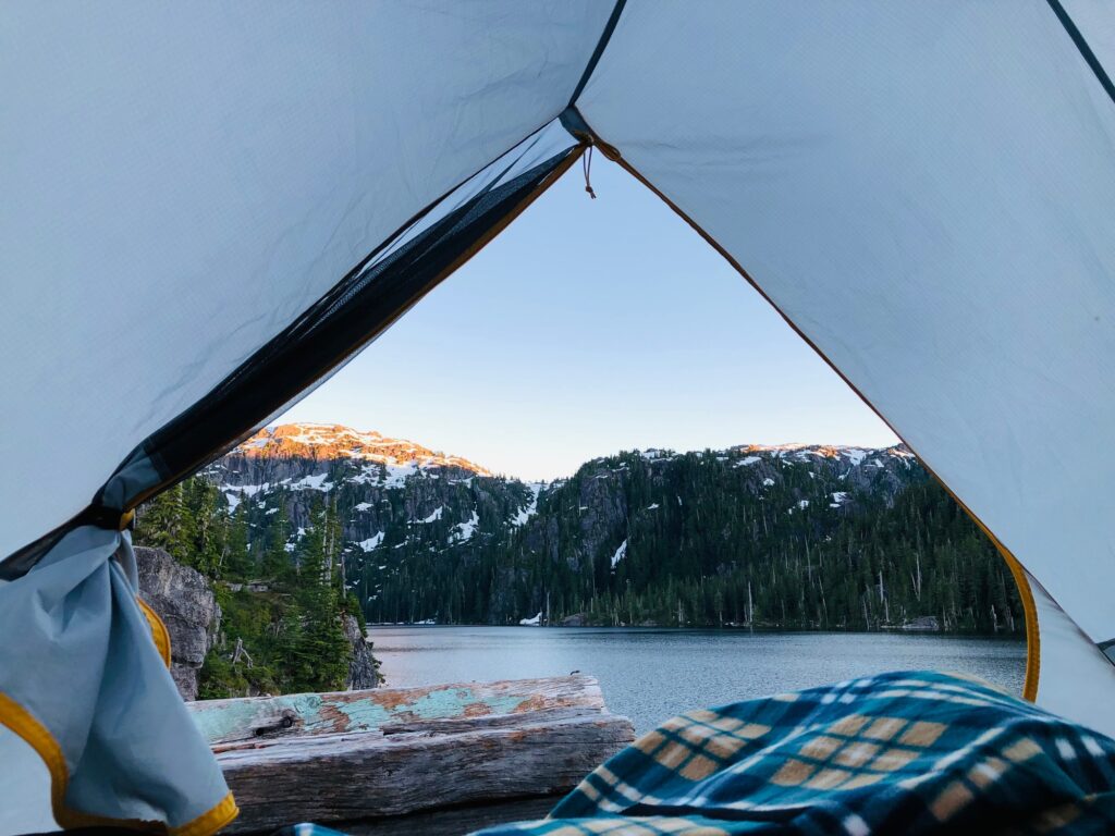 Camping in tent view of the mountains at sunset over lake with plaid blanket