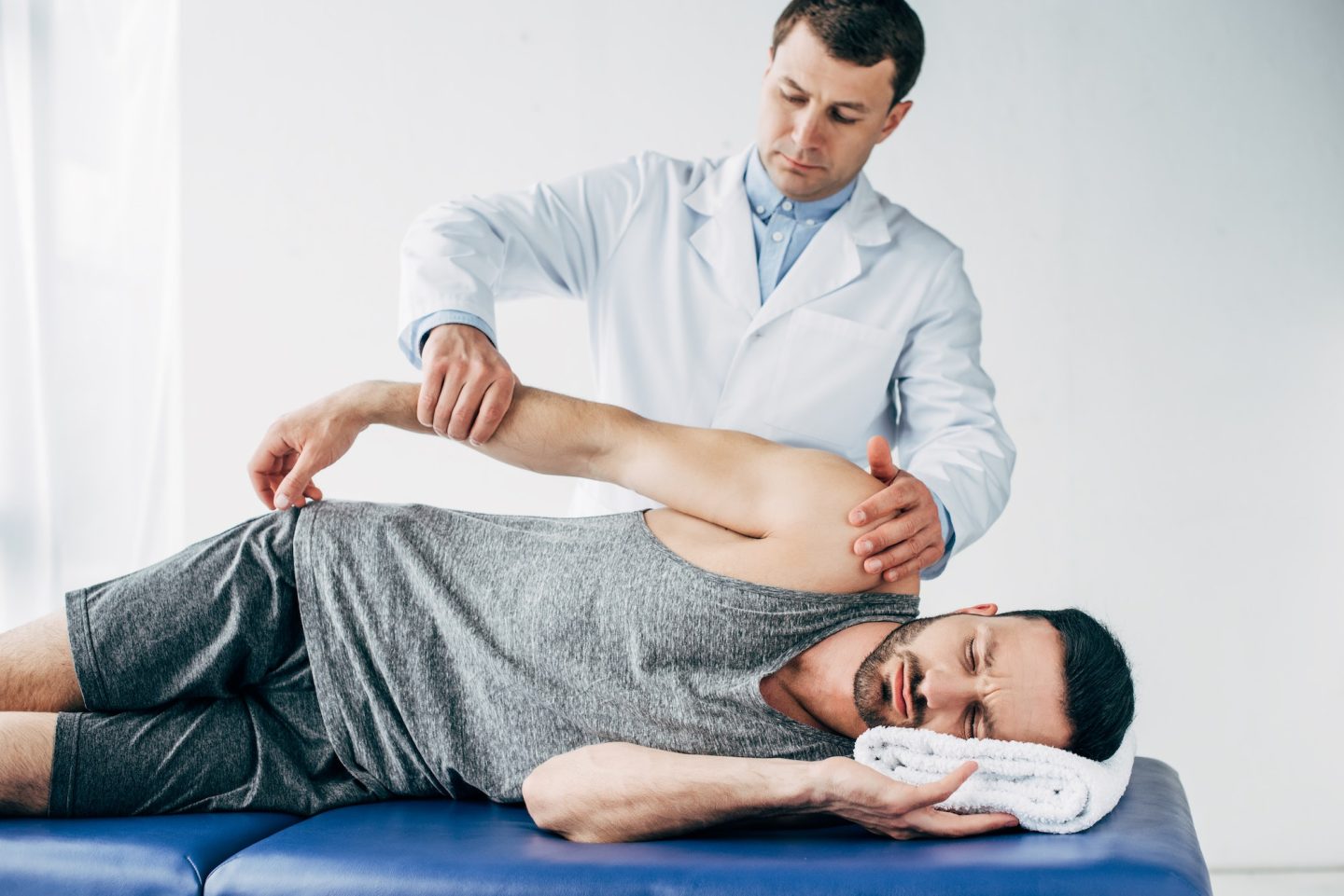 chiropractor stretching arm of handsome patient lying on massage table in hospital