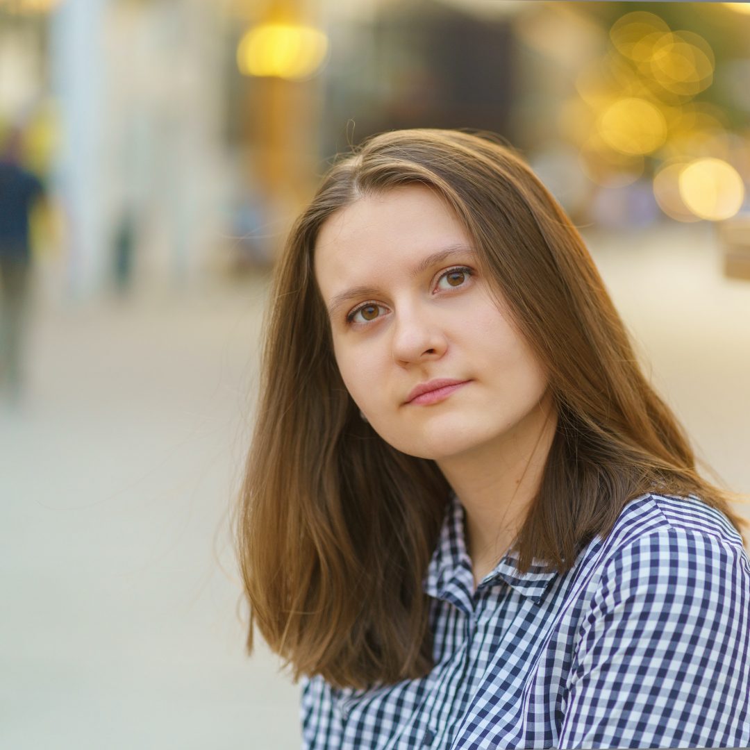 portrait of beautiful young woman with long blonde hair looking at camera against city view