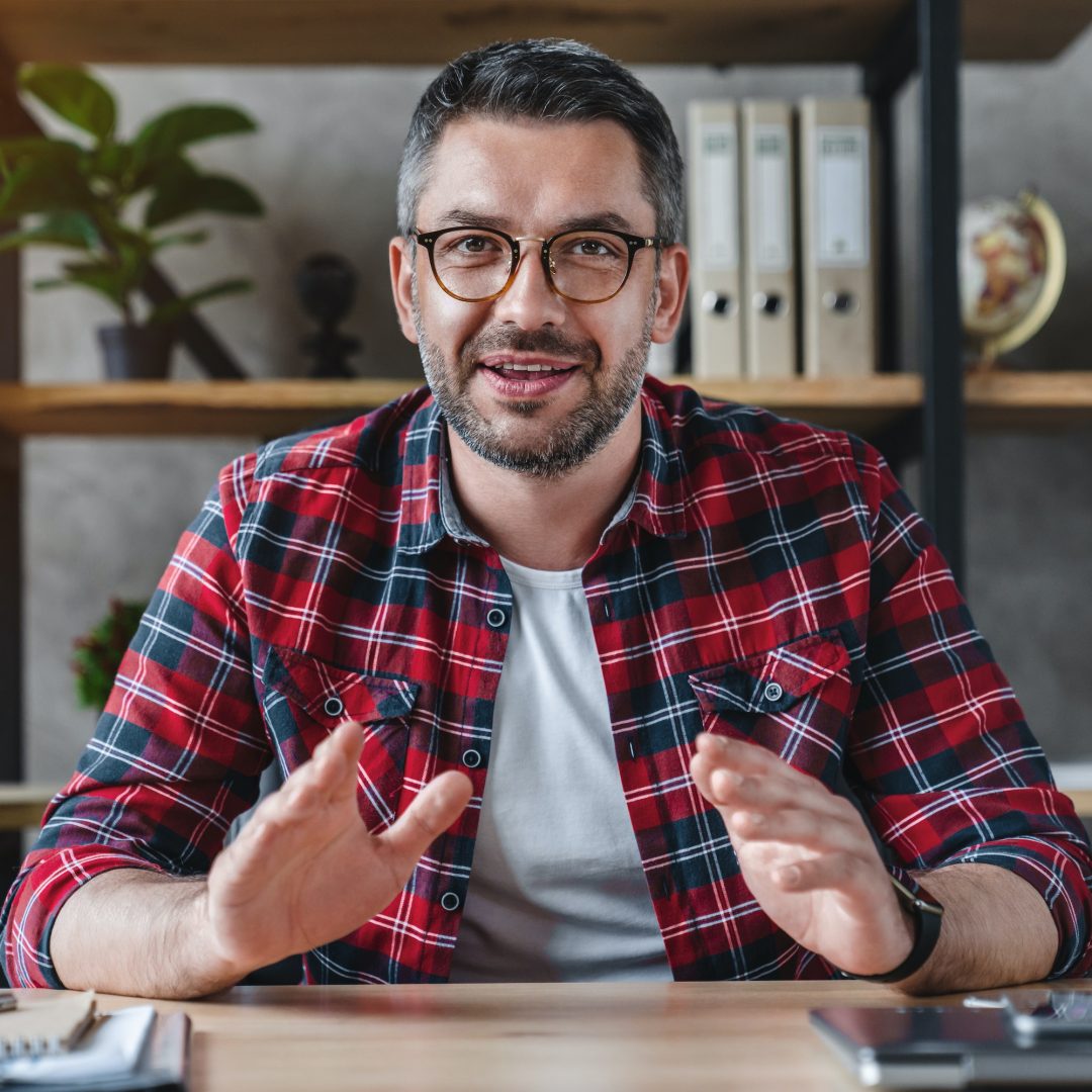 Smiling young businessman sit at desk talk on webcam having video call or conversation with client