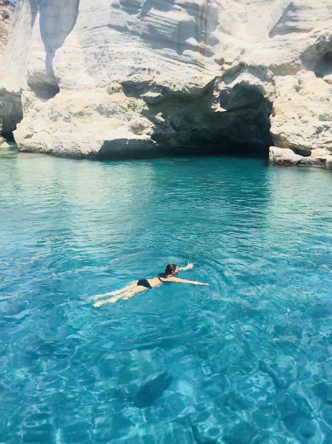Woman swimming in blue ocean near cliffs and caves
