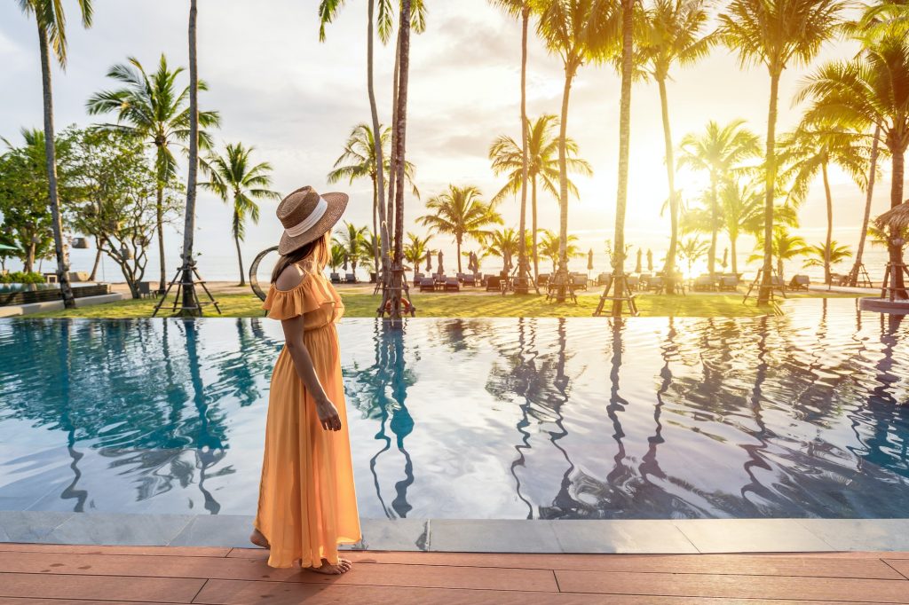 Young woman traveler relaxing and enjoying the sunset by a tropical resort pool while traveling