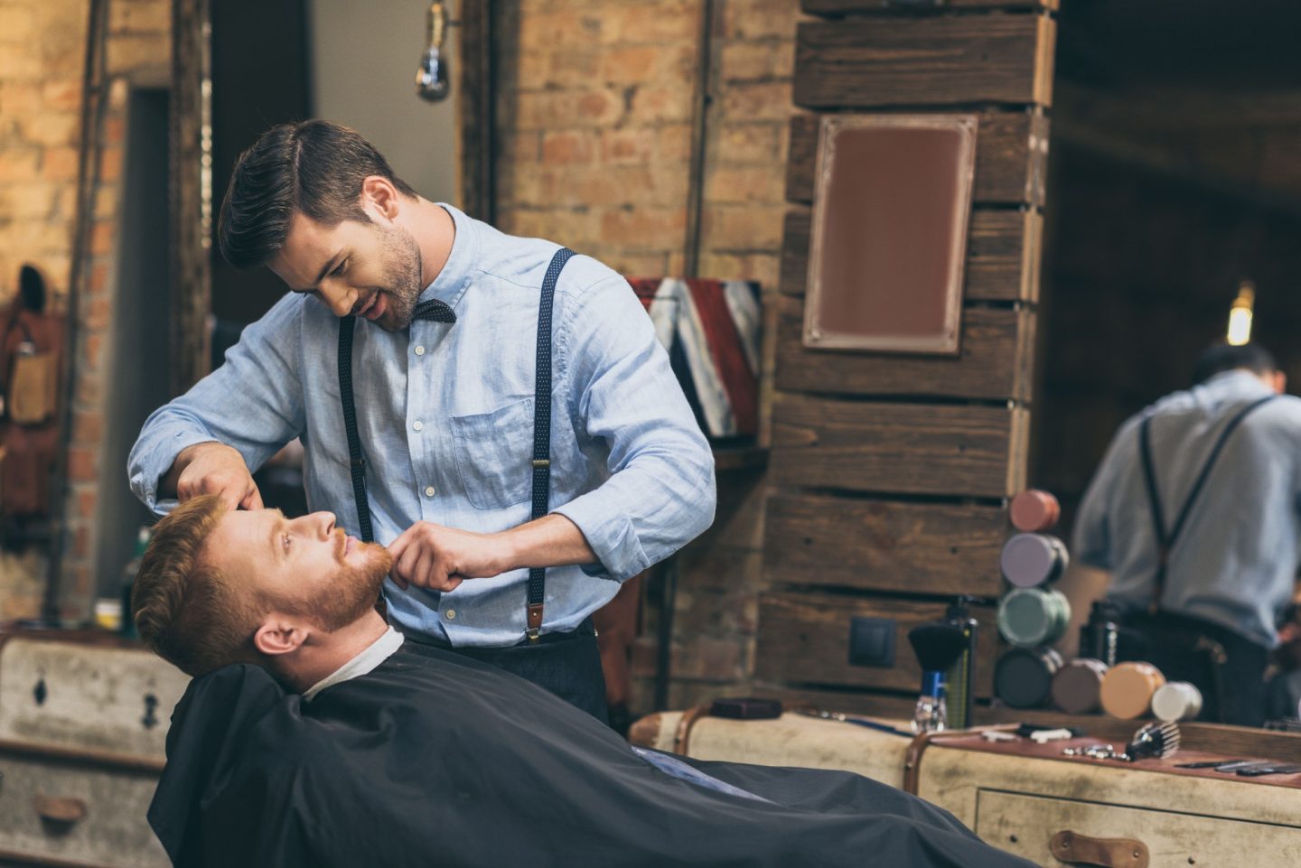 Male barber trimming customers beard in barber shop