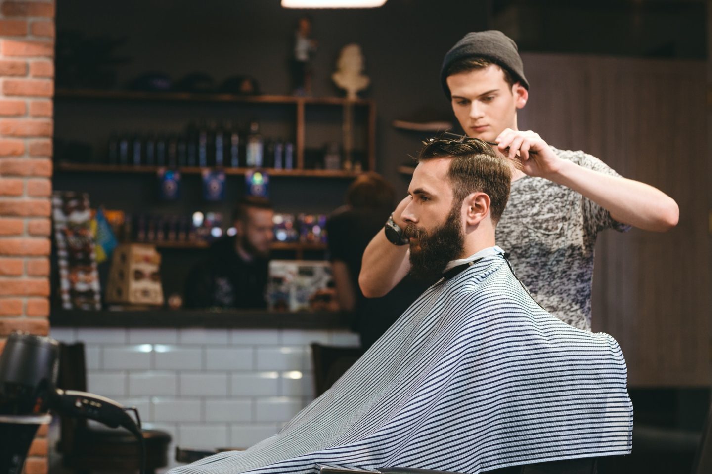 Young barber making haircut of bearded man in barbershop