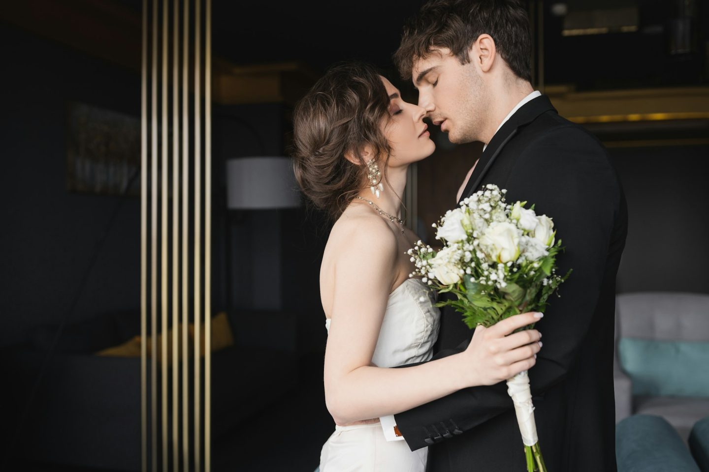 side view of good looking groom in black formal wear kissing brunette bride in elegant wedding