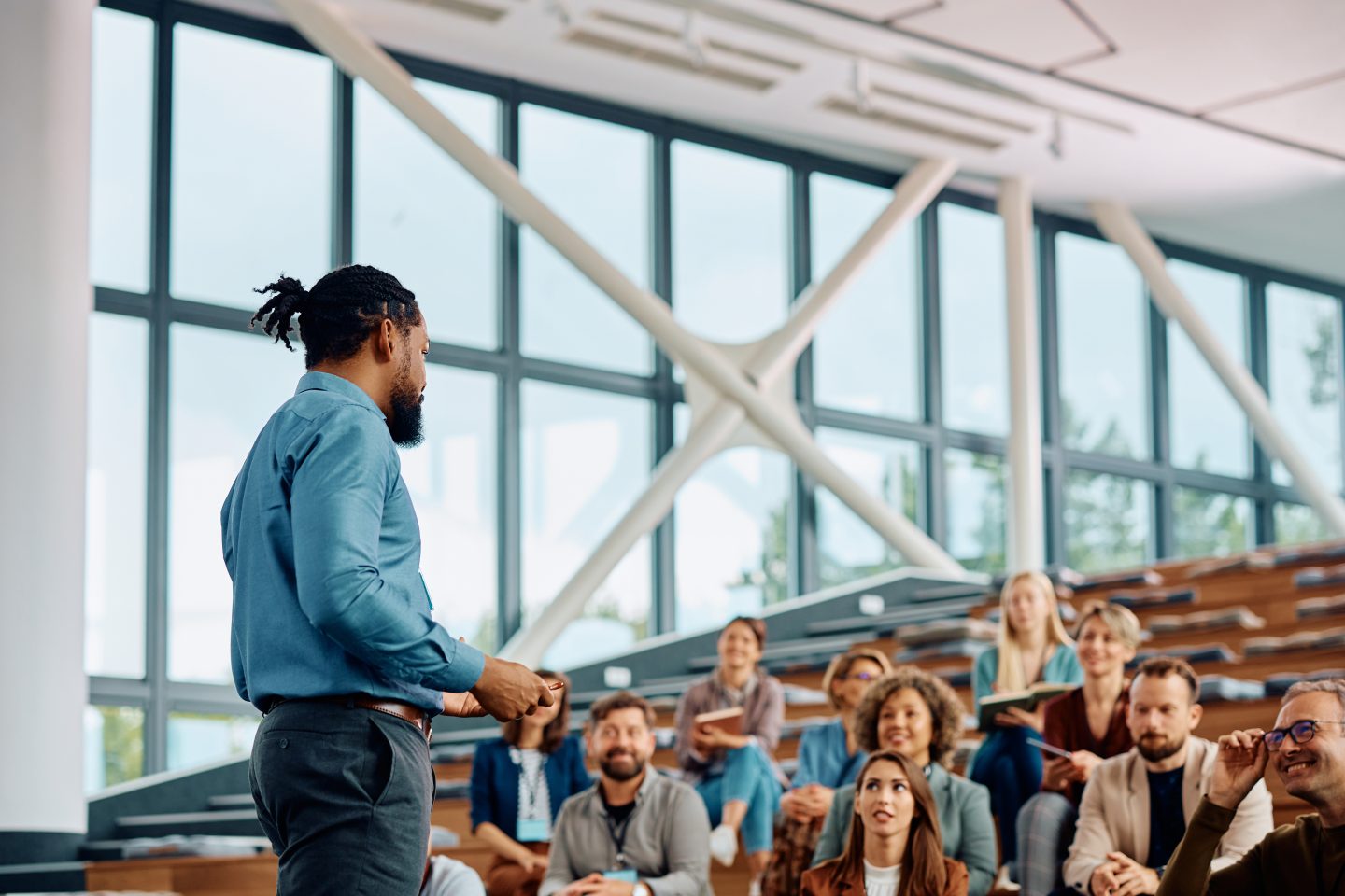 Black businessman talking to group of seminar attendees in conference hall.