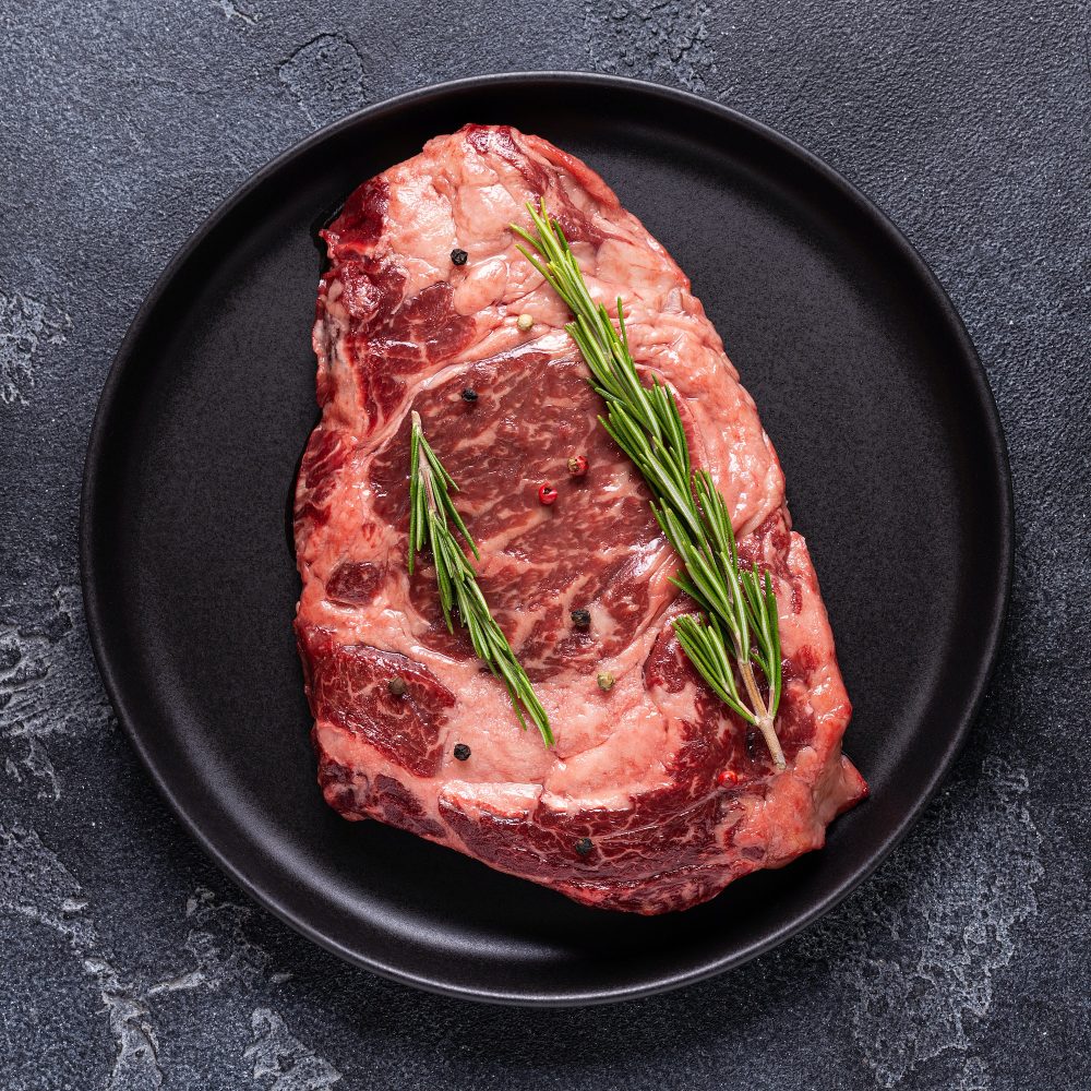 Fresh raw beef steak on black plate.