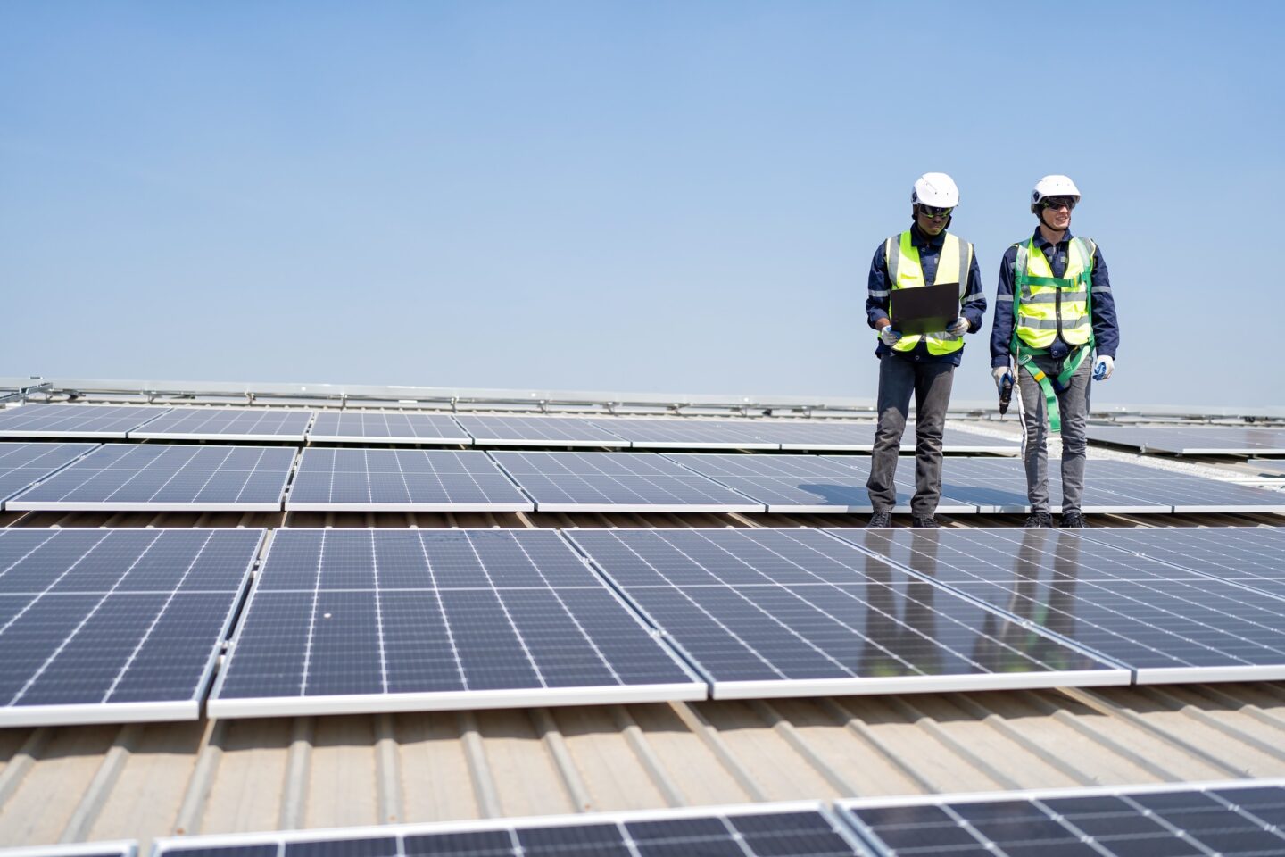 Engineer on rooftop stand next to solar panels discussion with team check laptop for installation
